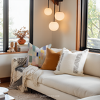 Cozy living room with a beige sofa adorned with colorful pillows and a blanket, near large windows.